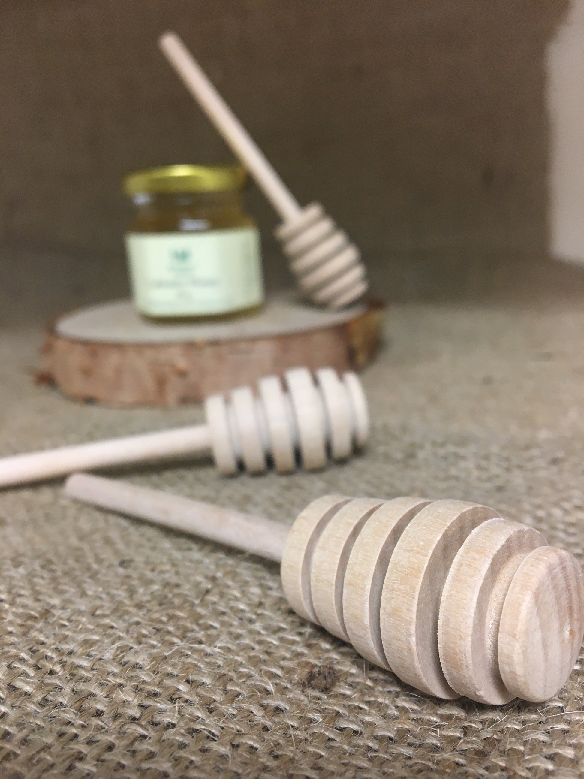 Small wooden honey dippers with small jar of honey in background